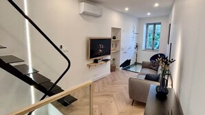 A modern interior with a staircase, a flat-screen TV, a sofa, and a dining table.