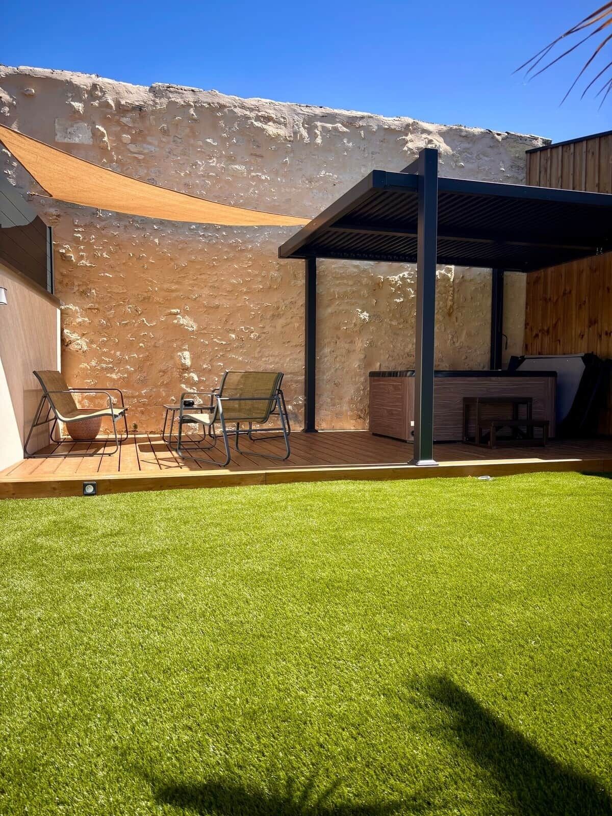 Eine Terrasse mit Tisch und Stühlen, ein überdachter Sitzbereich und eine Rasenfläche.