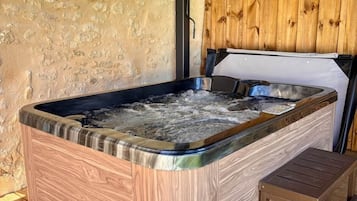 A hot tub with a wooden exterior, a wooden bench, and a stone wall.