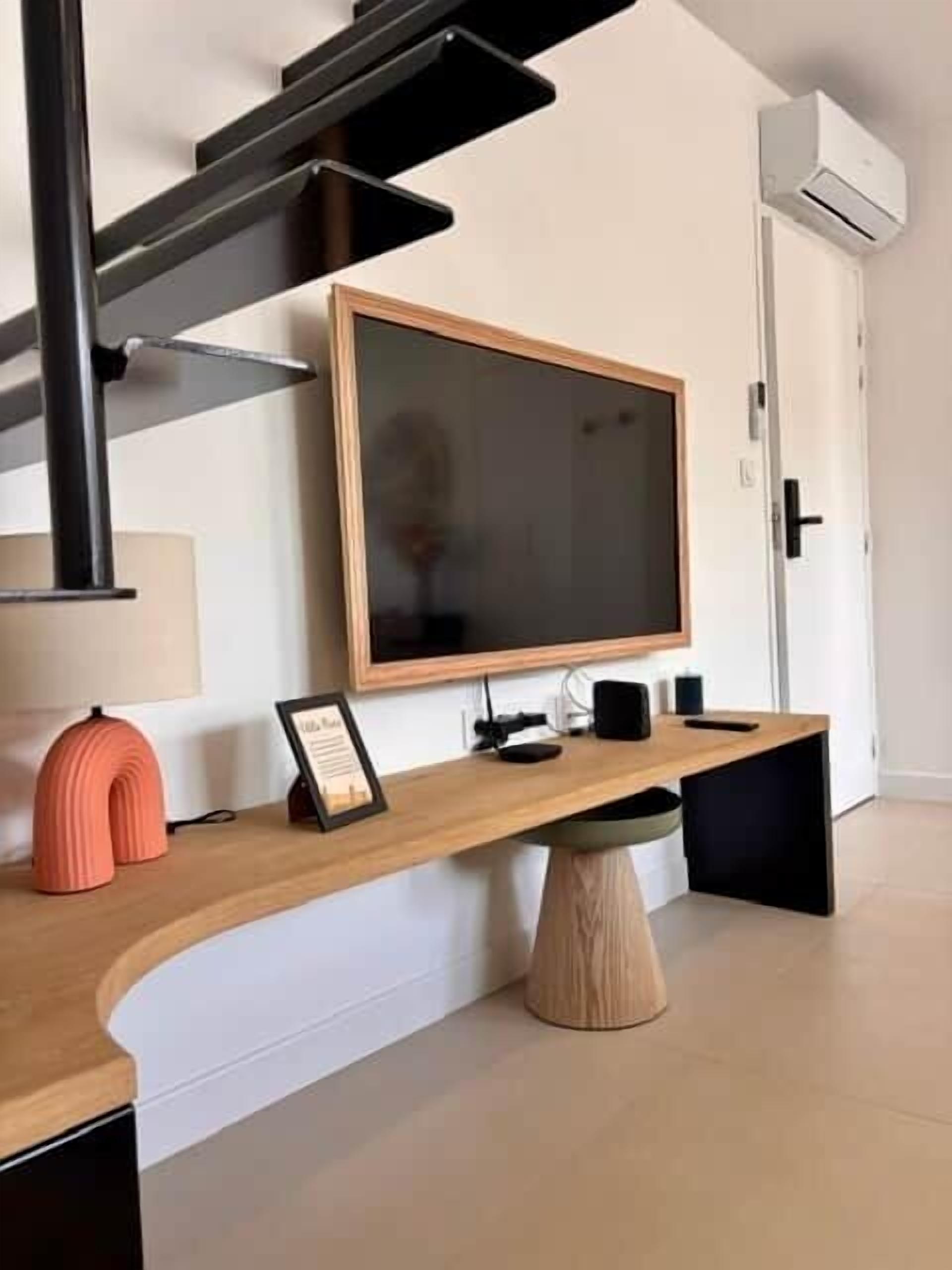Un saló modern amb un escriptori de fusta corbat, un televisor pla gran, un quadre emmarcat i una cadira negra.