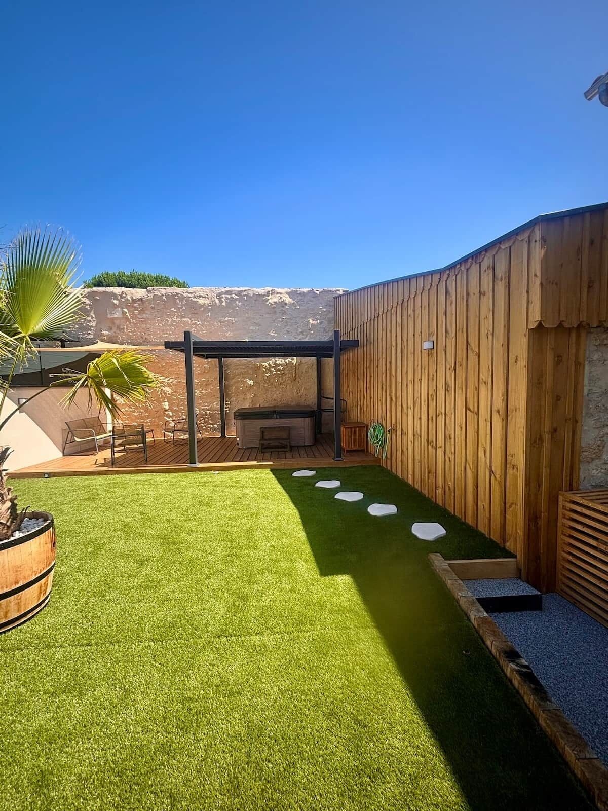 Un jardin avec une pelouse artificielle, un jacuzzi et une pergola en bois.