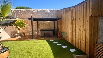 Un jardin avec une pelouse artificielle, un jacuzzi et une pergola en bois.