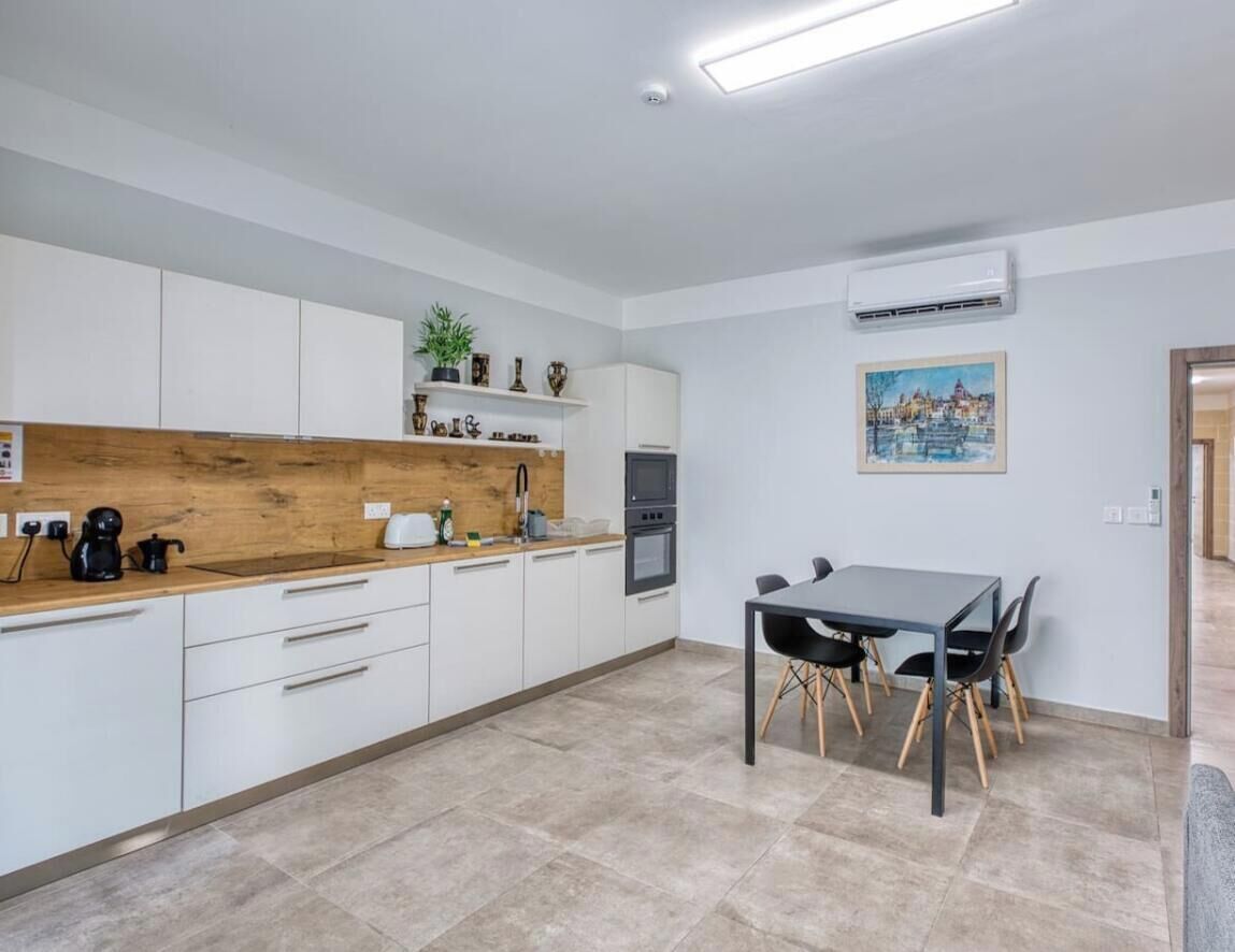 A modern kitchen with white cabinets, a wooden countertop, and a dining area with a table and chairs.