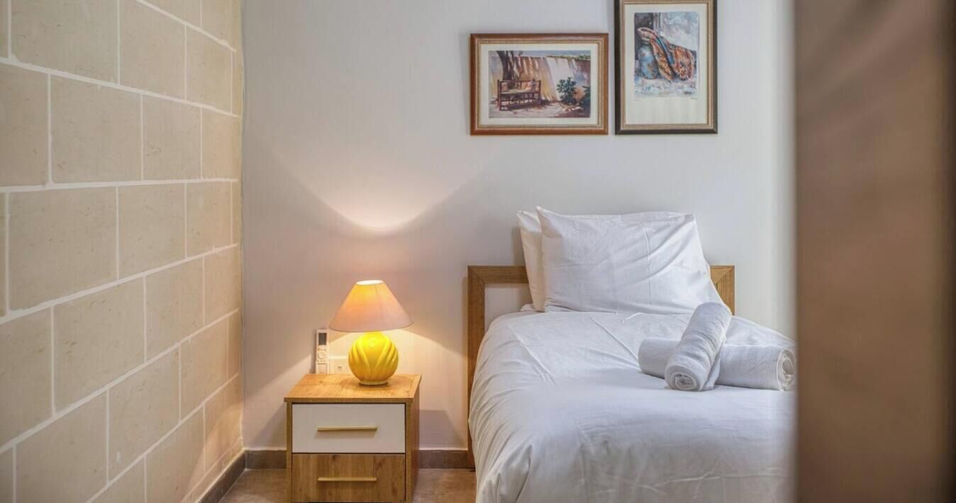 Een hotelkamer met een bed, een nachtkastje met een lamp, en twee afbeeldingen in lijsten aan de muur.