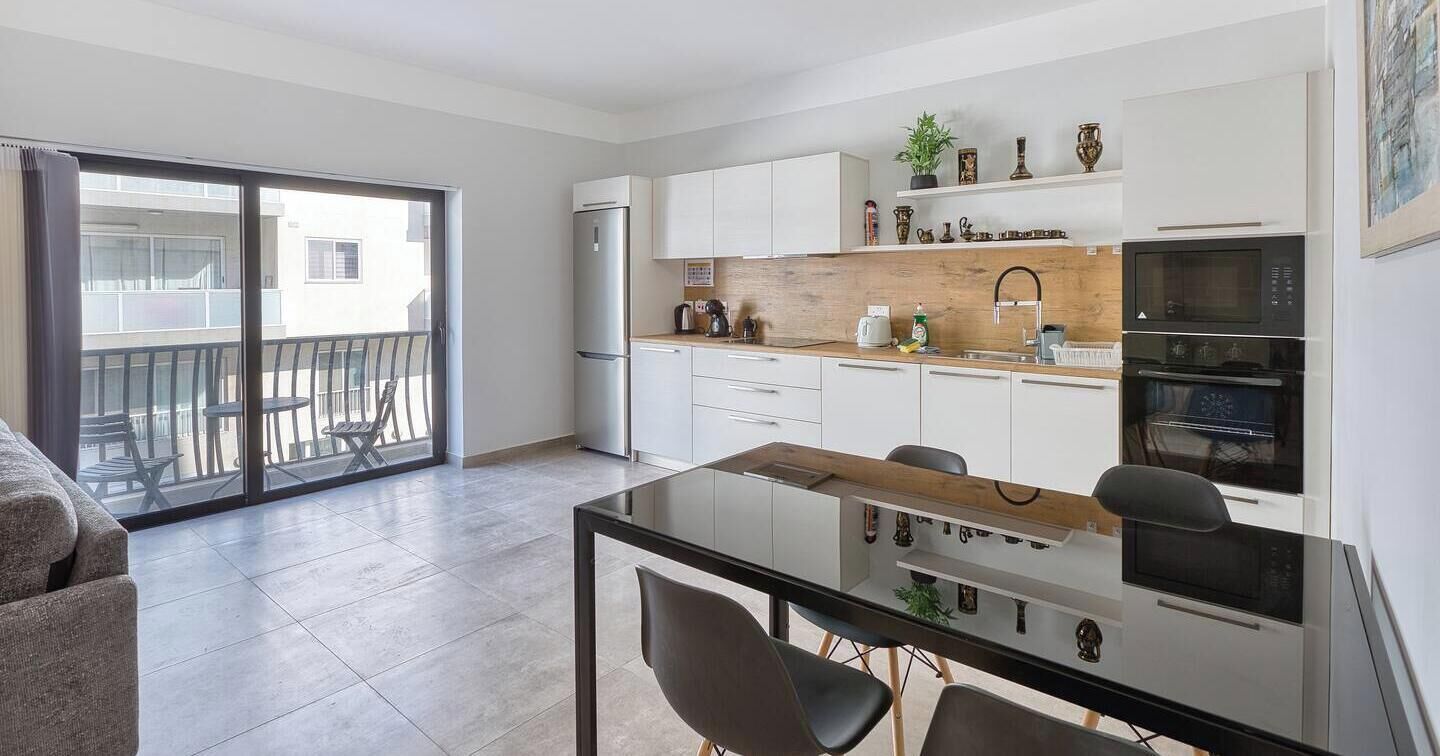 A modern kitchen with white cabinets, a wooden countertop, and a dining area with a glass table and chairs.