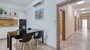 A modern kitchen with a dining area, a painting on the wall, and a hallway leading to another room. - 3BR Apartment with AC & Balcony in Marsascala (Marsaskala)
