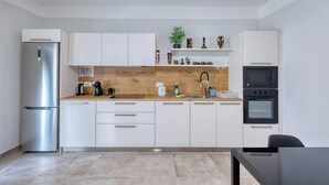 A modern kitchen with white cabinets, a stainless steel refrigerator, a wooden countertop, and a black oven. - 3BR Apartment with AC & Balcony in Marsascala (Marsaskala)