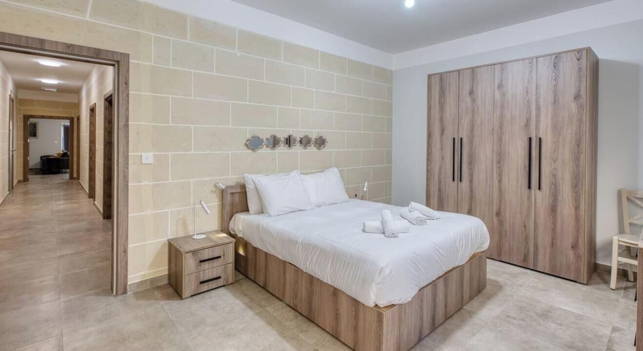 Een slaapkamer met een bed, nachtkastjes, een garderobe en een gang naar een andere kamer.