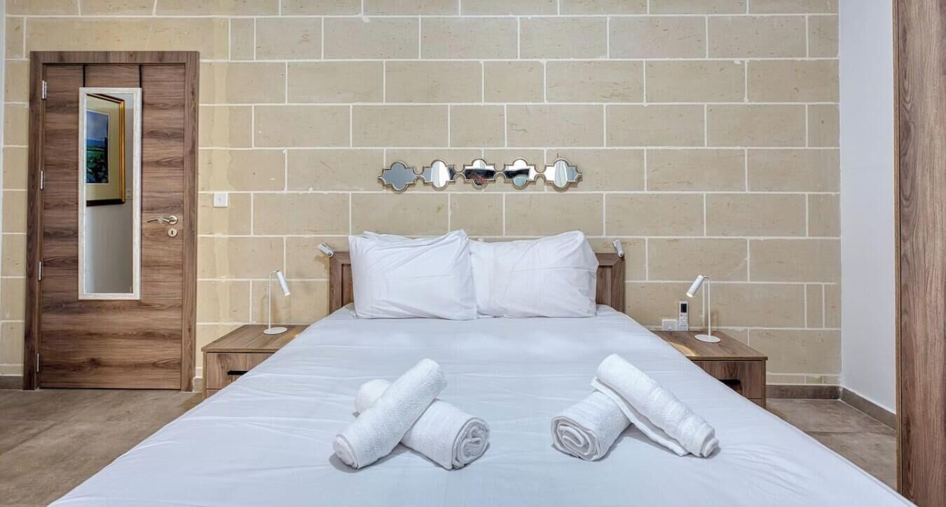 Una habitación de hotel con una cama grande, dos mesitas de noche, una puerta de madera y un espejo adosado a la pared.