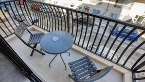 A balcony with a table and chairs, a metal railing, and a view of parked cars and buildings. - 3BR Apartment with AC & Balcony in Marsascala (Marsaskala)