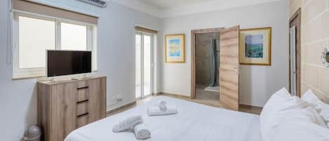 A hotel room with a bed, a TV, a wooden dresser, a window, and a door leading to a shower area.
