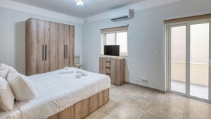 A bedroom with a bed, wardrobe, TV, and a sliding door to a balcony. - 3BR Apartment with AC & Balcony in Marsascala (Marsaskala)