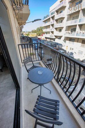 A balcony with a round table and two chairs, a railing, and a view of a multi-story building with balconies. - 3BR Apartment with AC & Balcony in Marsascala (Marsaskala)