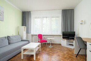 A living room with a sofa, a coffee table, a TV, a desk, and a chair. - RentPlanet - Apartament Orla (Warszawa)
