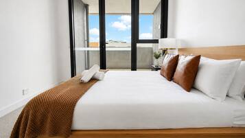Una habitación de hotel con una cama, una mesita de noche, una lámpara y vistas a través de una puerta corrediza.