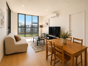 A modern living room with a sofa, TV, dining table, and chairs. - Modern 2BR2BA Apt in Clayton South Parking WIFI (Clayton south)