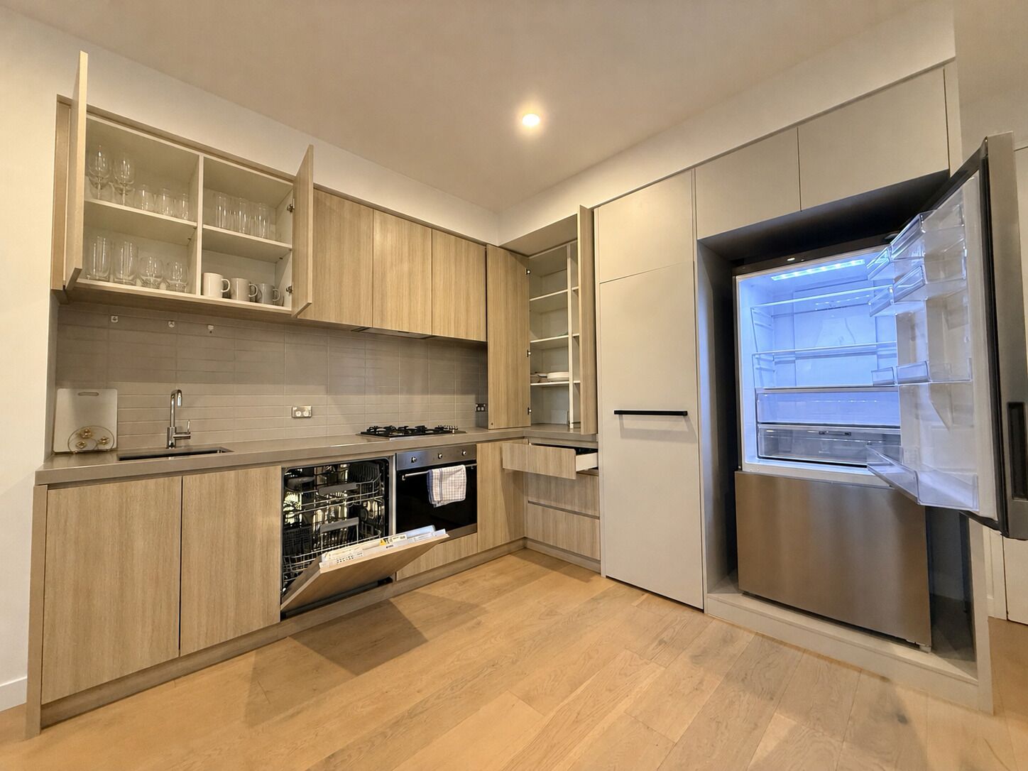 Eine moderne Küche mit Holzschränken, einem eingebauten Backofen, einem Geschirrspüler und einem Edelstahl-Kühlschrank.