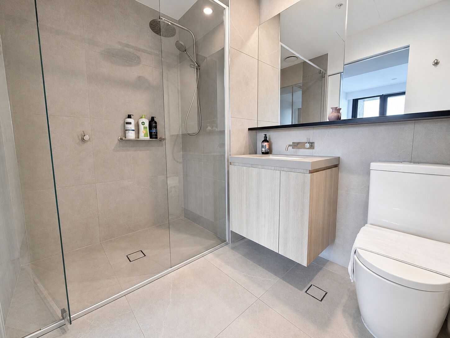 Un baño moderno con ducha envuelta en vidrio, tocador de madera y un inodoro blanco.