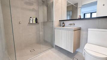 Un baño moderno con ducha envuelta en vidrio, tocador de madera y un inodoro blanco.