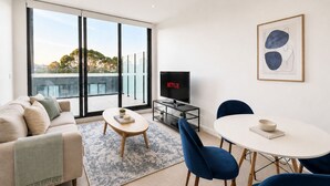 Uma sala de estar moderna com sofá, mesa de centro, televisão e um espaço de jantar com cadeiras e mesa.