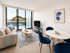 A modern living room with a sofa, a coffee table, a TV, and a dining area with chairs and a table. - Clayton 2BR1BA Apt Near Monash WIFI Parking (Clayton)