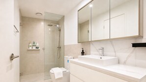 A modern bathroom with a glass shower enclosure, a white sink, and a large mirror.