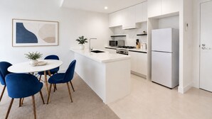 A modern kitchen with white cabinetry, a central island, and a dining area with blue chairs.