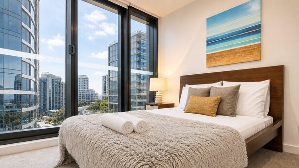 A modern bedroom with a large window, a bed with a fluffy blanket, and a city view.