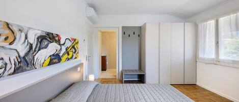 A bedroom with a bed, a painting on the wall, a wardrobe, and a window.