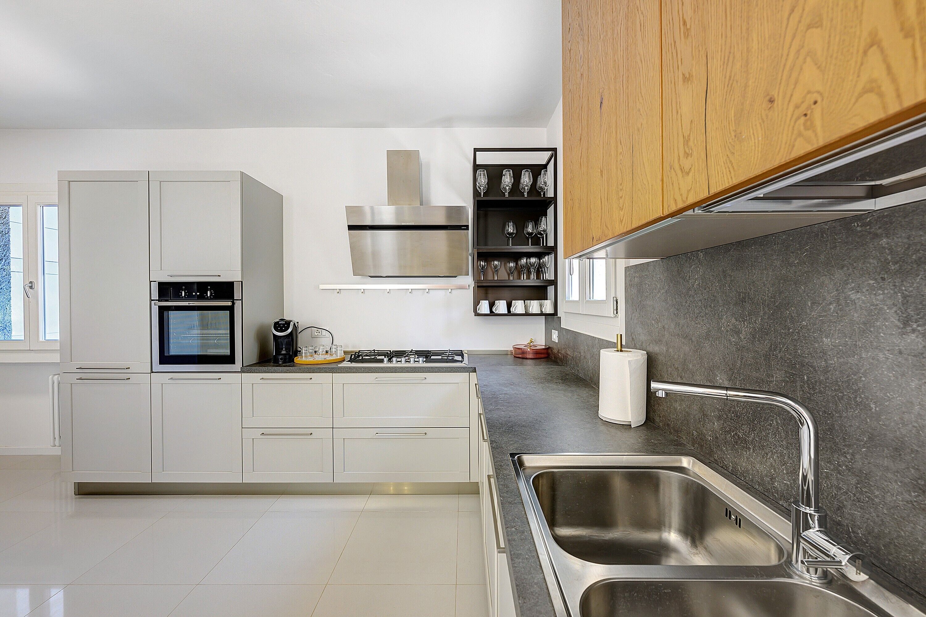 Una cucina moderna con mobili bianchi, un lavello in acciaio inossidabile e un forno integrato.