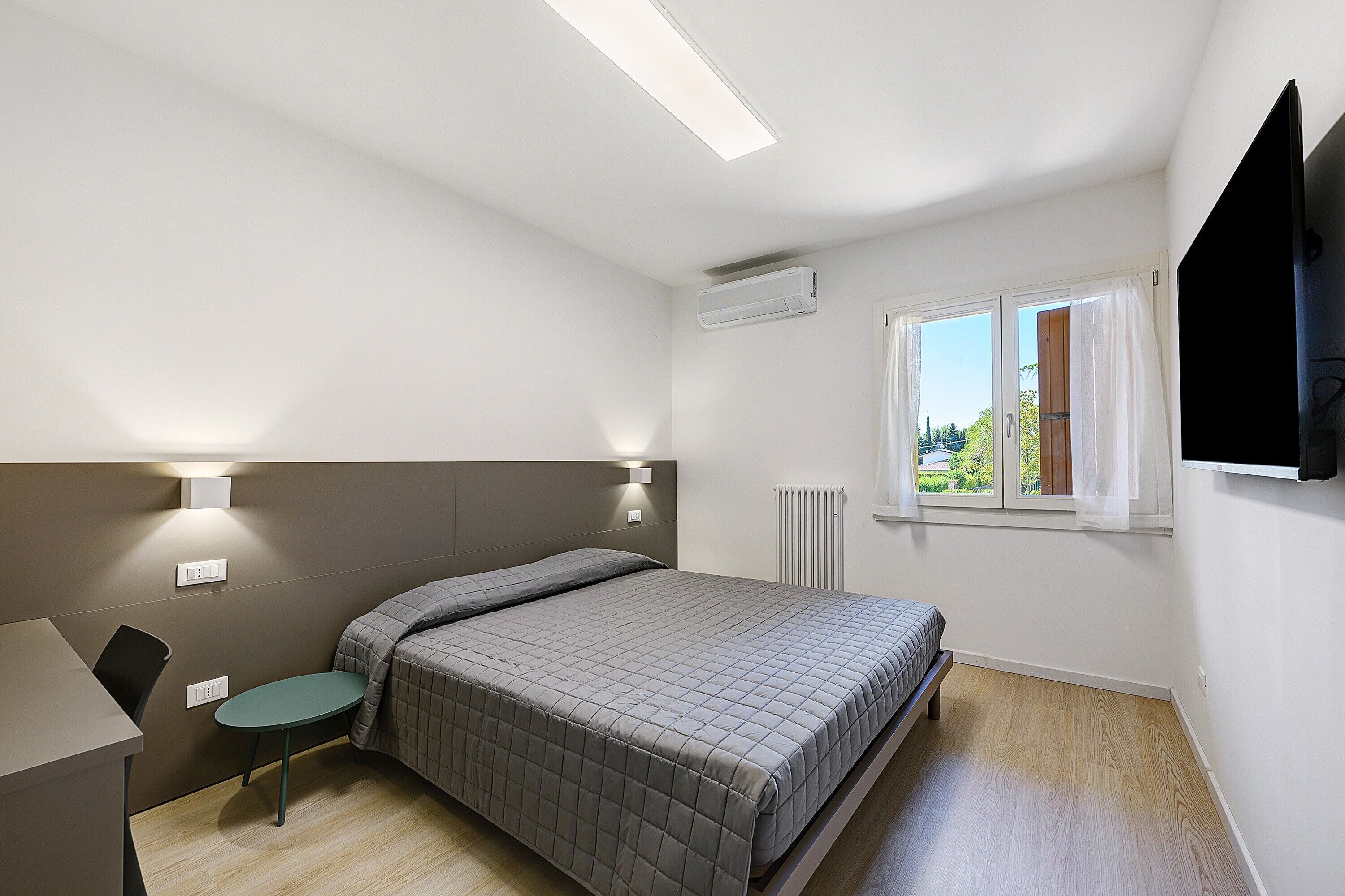 A bedroom with a bed, bedside table, chair, and a window with curtains.