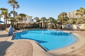 A swimming pool with a curved edge, surrounded by palm trees and a building with a light-colored facade. - Beach Resort Getaway | Private Beach Access | Sleeps 6 | Resort Pools (Destin)
