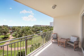 A balcony with a view of a landscaped area, a chair, and a small table. - Beach Resort Getaway | Private Beach Access | Sleeps 6 | Resort Pools (Destin)