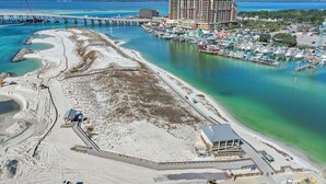 Luftaufnahme einer Küstenlandschaft mit einem Yachthafen, einem großen Hotel und einem Strand mit Bauarbeiten.