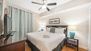 Ein Hotelzimmer mit einem Bett, zwei Nachttischen, einem Deckenventilator, einem Fenster mit Vorhängen und einem Wandbild.