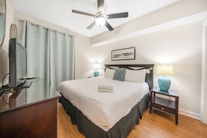 A hotel room with a bed, two bedside tables, a ceiling fan, a window with curtains, and a wall-mounted artwork. - Beach Resort Getaway | Private Beach Access | Sleeps 6 | Resort Pools (Destin)