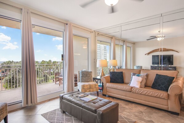 Ein geräumiges Wohnzimmer mit einer großen Couch, einem Couchtisch und einem Balkon mit Blick auf Palmen.