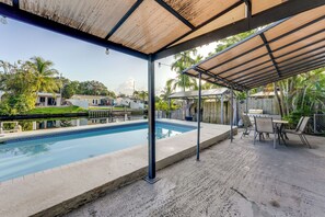 A covered outdoor area with a swimming pool, patio furniture, and a view of residential buildings.