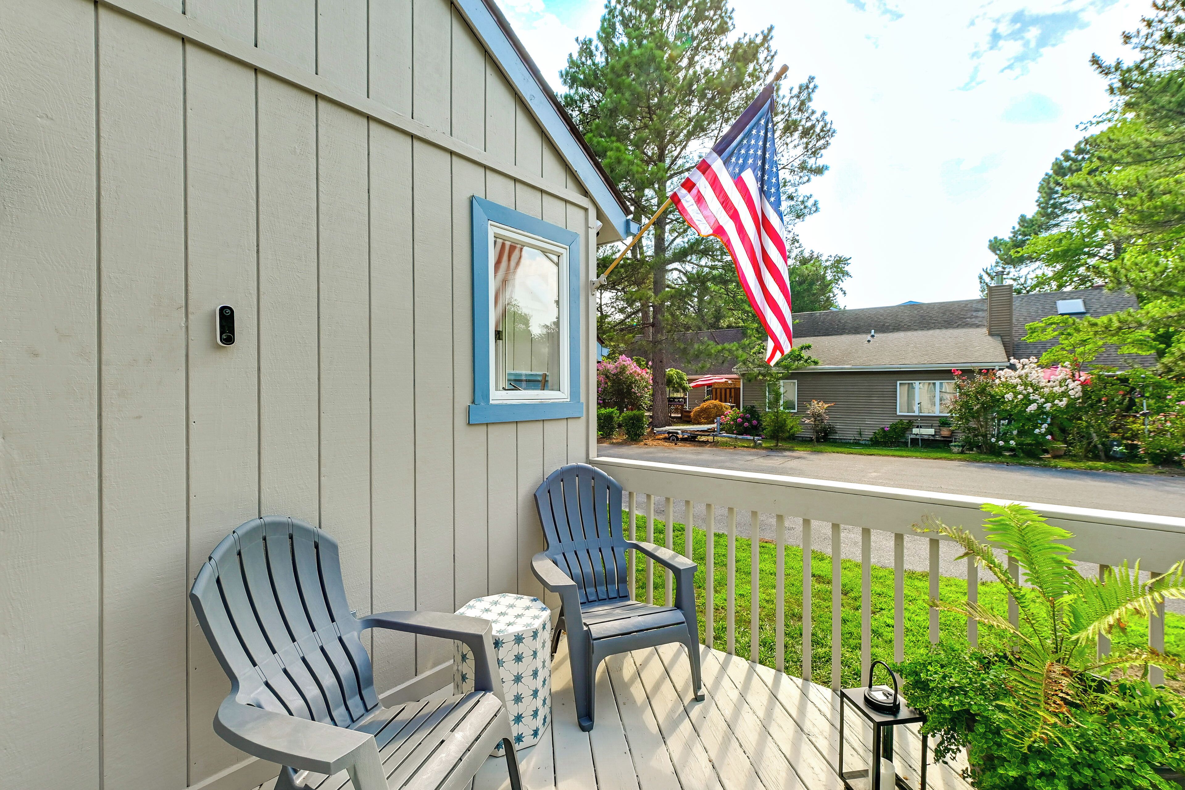 A porch with two Adirondack chairs, a small table, and an American flag.
