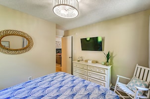 Un dormitorio con cama, cómoda, televisor, silla y espejo.