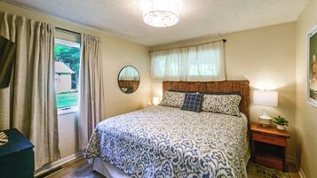 A bedroom with a bed, a bedside table with a lamp, a mirror, and a window with curtains.