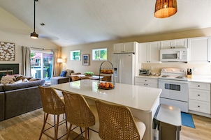 A modern kitchen with white cabinets, a central island with bar stools, a microwave, and a stove.