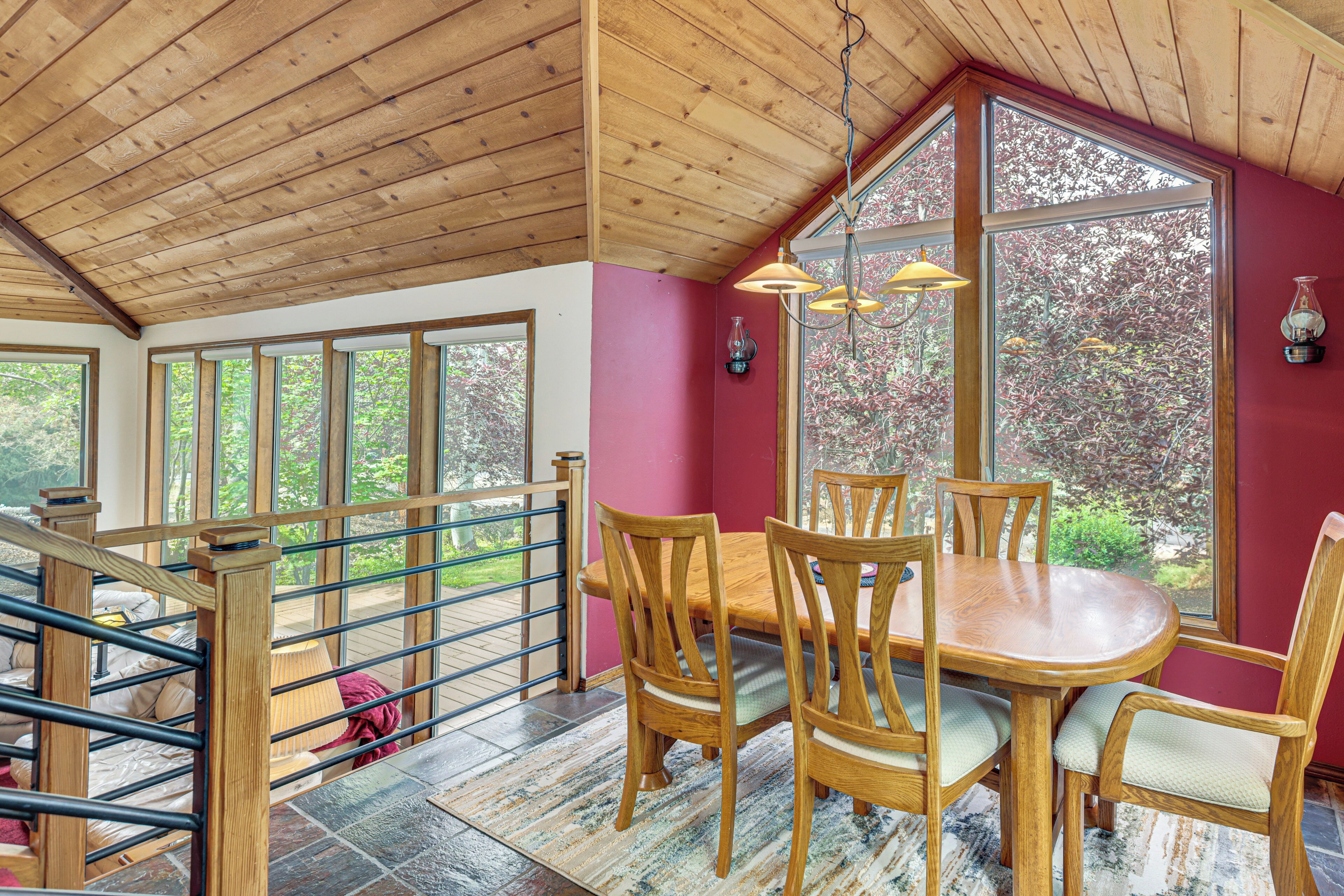 A dining area with a wooden table and chairs, large windows, and a wooden ceiling.