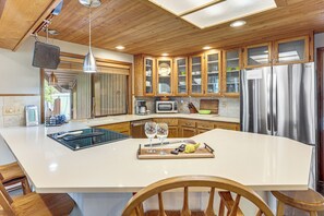 A kitchen with wooden cabinets, a large island, stainless steel appliances, and a dining area with a wooden table and chairs. - Fire Pit & Wildlife Views! Tranquil Bend Retreat (Bend)