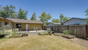 A residential backyard with a house, a wooden fence, and various potted plants.