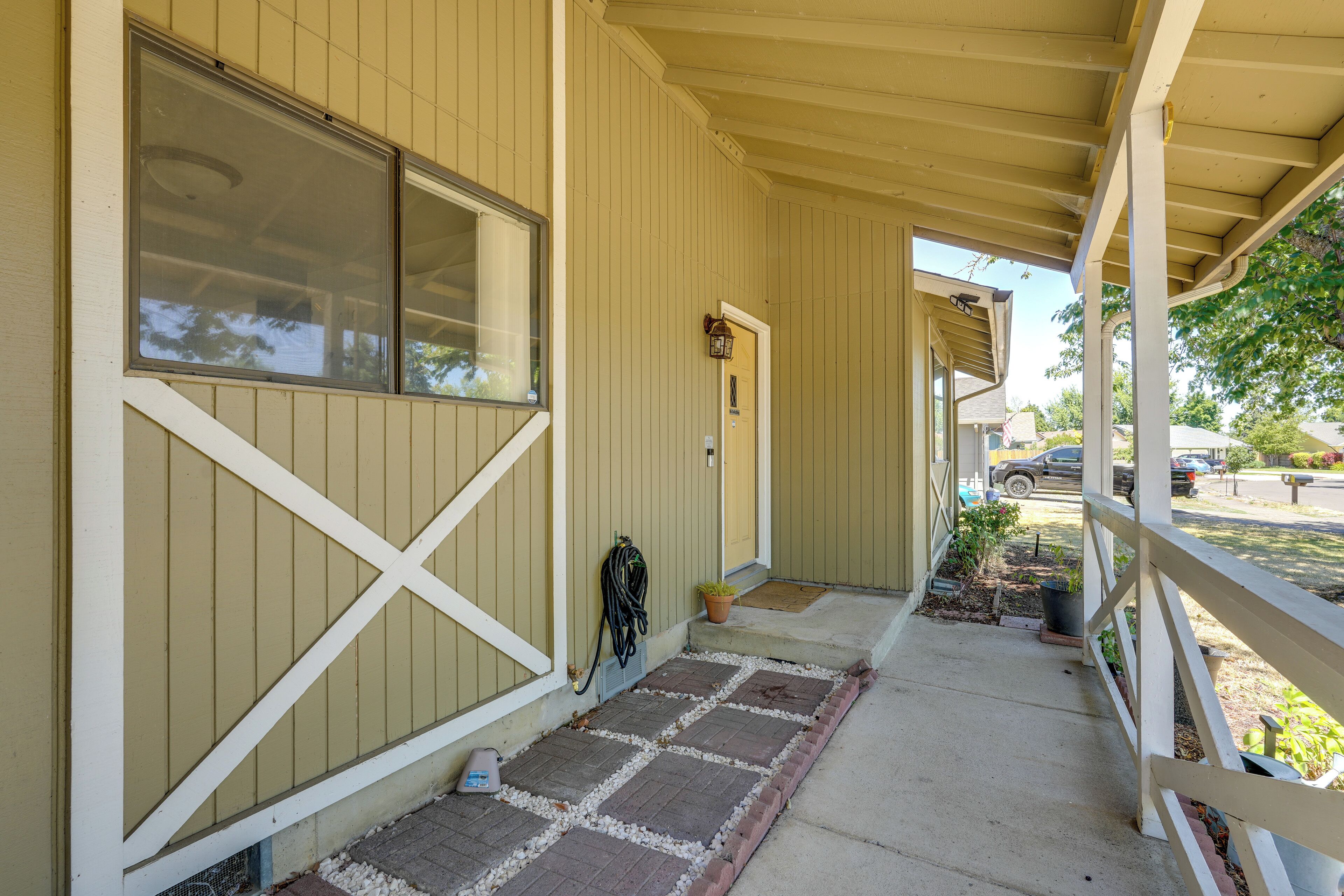 A covered porch with a brick pathway leading to a door, a mailbox, and a hose on the wall.