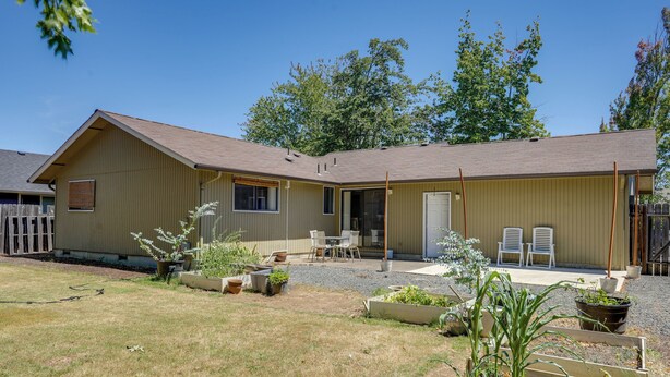 A single-story house with a front porch, a small garden area with plants and a wooden bench, and a clear sky.