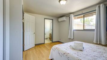 A bedroom with a bed, a door, a window with curtains, and an air conditioning unit.