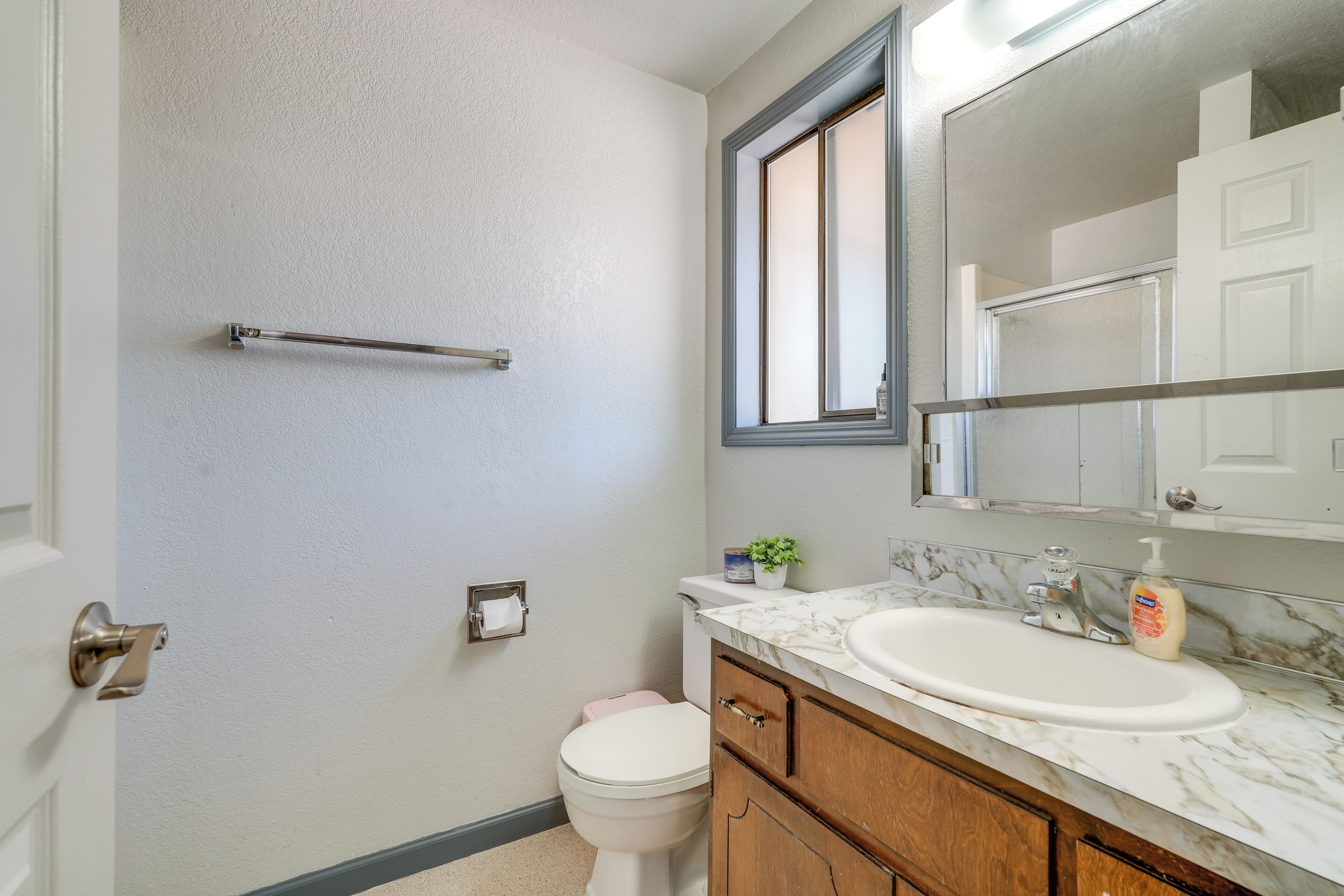 A bathroom with a white toilet, a marble sink, a wooden cabinet, a towel rack, and a window.