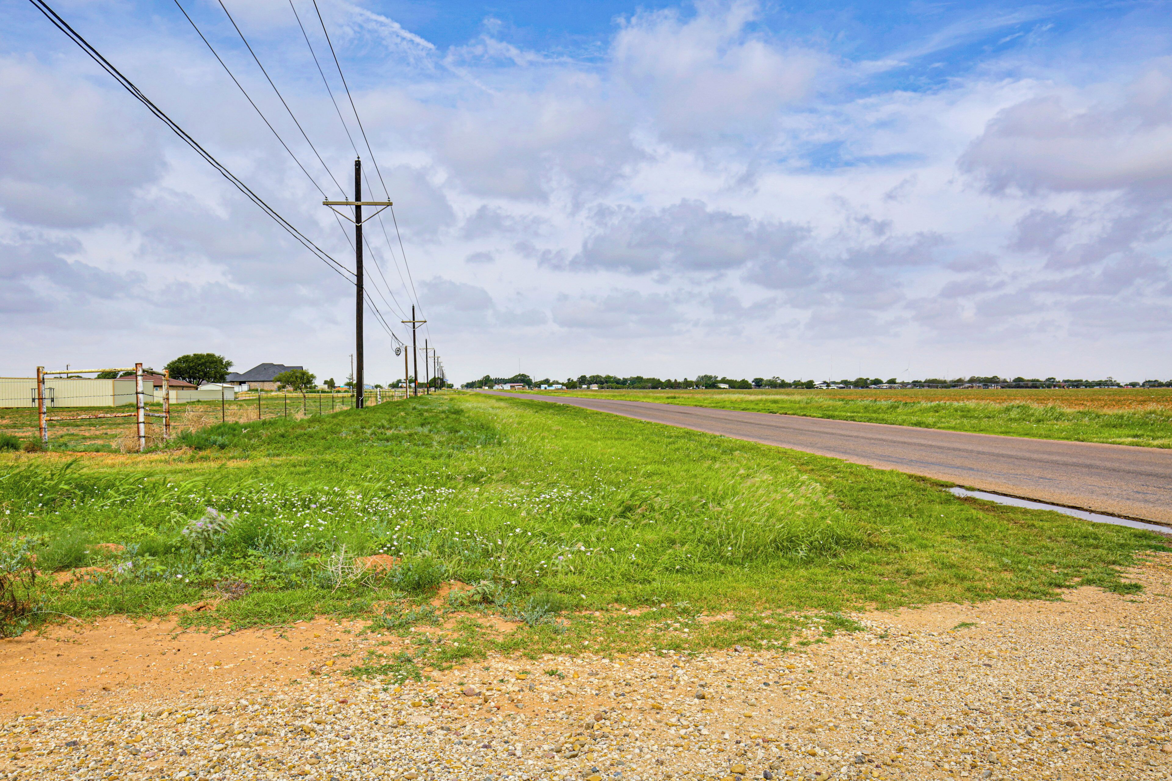 A rural road with a fence, utility poles, and a clear sky.